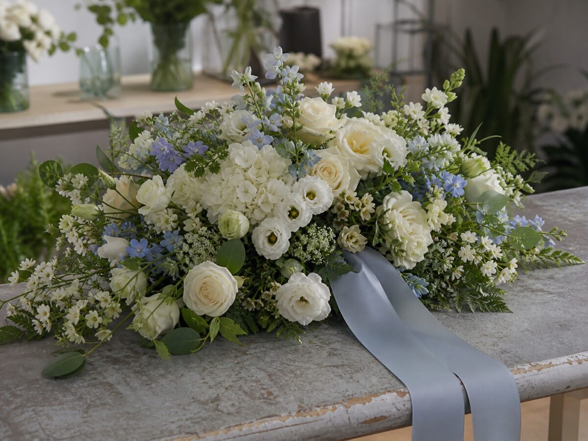 Würdevolles Trauergesteck in Weiß Creme und zartem Blau auf einem Floristentisch