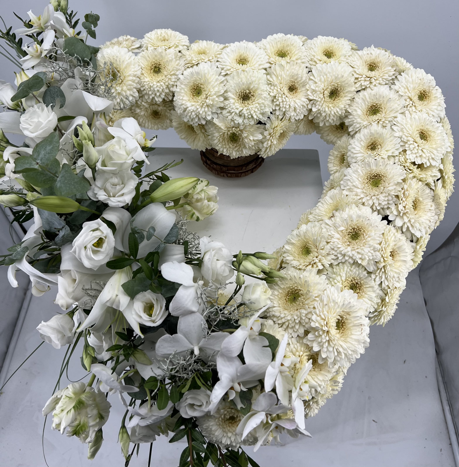 Großer floraler Anker aus weißen Blüten, Lilien und Eukalyptus vor einem hellgrauen Hintergrund.