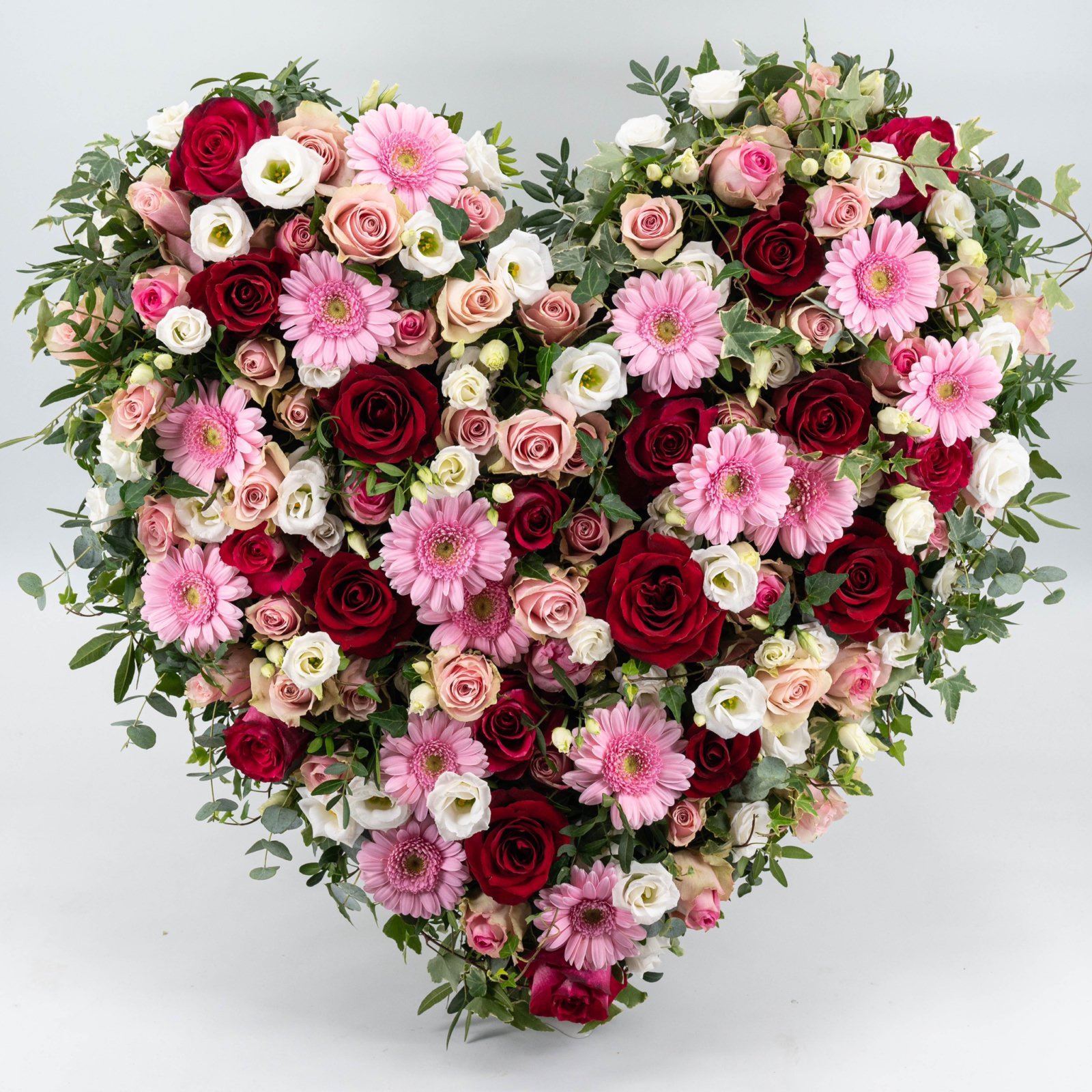 Üppiges Blumenherz aus roten und rosafarbenen Rosen, rosa Gerbera, weißen Blüten und lockerem Grün.
